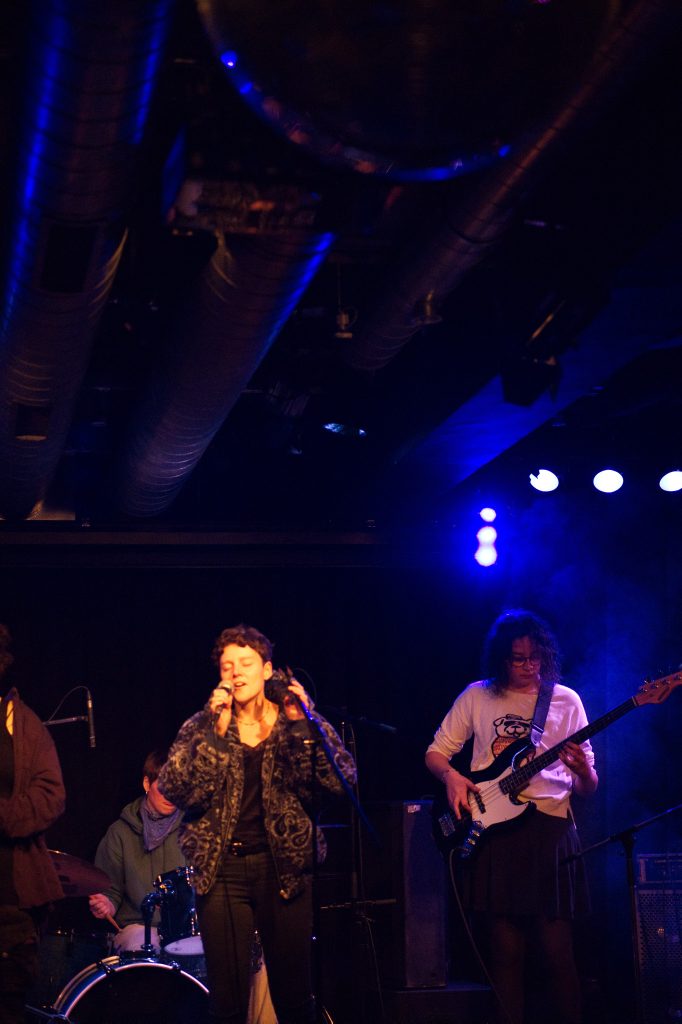 Musikalische Performance bei einer Jam Session. Mehrere Personen musizieren auf der Bühne, begleitet von stimmungsvoller Bühnenbeleuchtung